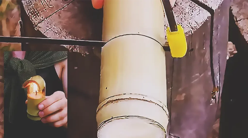 A handmade waterproof bamboo candle with melted blue wax, a cord wick, and foil reflector being lit outdoors for camping and bushcraft survival use.