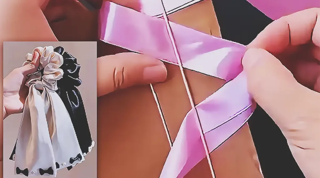 A handmade satin ribbon scrunchie hair tie with ruched pink ribbon, long ribbon tails, and a small gold charm, made using elastic bands and a cardboard frame.